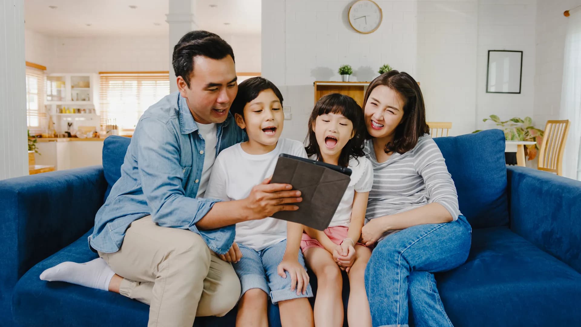 Asian family smiling together while using a tablet at home